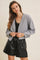 woman wearing a gray cropped cardigan over a black tank top and black faux leather shorts