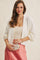 woman wearing a cream cardigan over a beige tank top and holding a white clutch, paired with a pink satin skirt