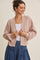 woman wearing a light pink cropped cardigan over a white top with a layered necklace and denim skirt