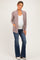 woman wearing a light mauve maternity cardigan over a white top and blue flared jeans, showing her baby bump
