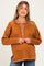 woman wearing a rusty orange maternity top with a button-front and ribbed texture, smiling at the camera