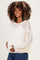 woman wearing a cream open knit maternity sweater and showing her baby bump