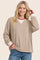 woman wearing a brown and white striped long sleeve top with red collar and cuffs, smiling while posing