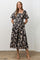 woman wearing a black floral midi dress with puff sleeves and a smocked bodice, standing with hands in pockets