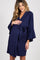 woman wearing a navy blue maternity robe and cradling her baby bump while kneeling on a bed