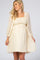 woman wearing a cream short maternity dress with smocked bodice and sheer sleeves, showcasing baby bump