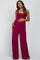woman wearing a fuchsia maternity jumpsuit with a smocked bodice and side pockets, holding her baby bump