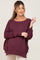 woman wearing a deep burgundy maternity sweater with a loose fit and rolled cuffs, showing a visible baby bump