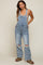 woman wearing a light wash maternity oversized denim overalls with distressed details and a fitted tank top underneath