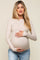 woman wearing a beige long sleeve maternity top and holding her baby bump