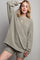 woman wearing an oversized light gray textured sweater with matching shorts and a gold pendant necklace