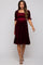 woman wearing a burgundy maternity dress with a smocked bodice and short puff sleeves, featuring a ruffle hem