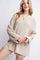 woman wearing a beige oversized knit sweater with long sleeves and a relaxed fit, styled with layered necklaces