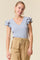 woman wearing a light gray short sleeve top with ruffle details and a v-neckline paired with beige pants