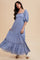 woman wearing a light blue maxi dress with puff sleeves and lace details, posing against a neutral background