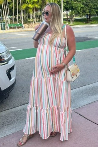 woman wearing a multicolored striped maternity maxi dress and holding her baby bump while standing outdoors