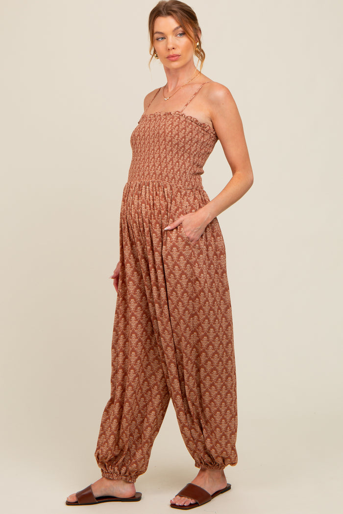 woman wearing a rust-colored maternity jumpsuit with a smocked bodice and wide-leg pants, featuring pockets