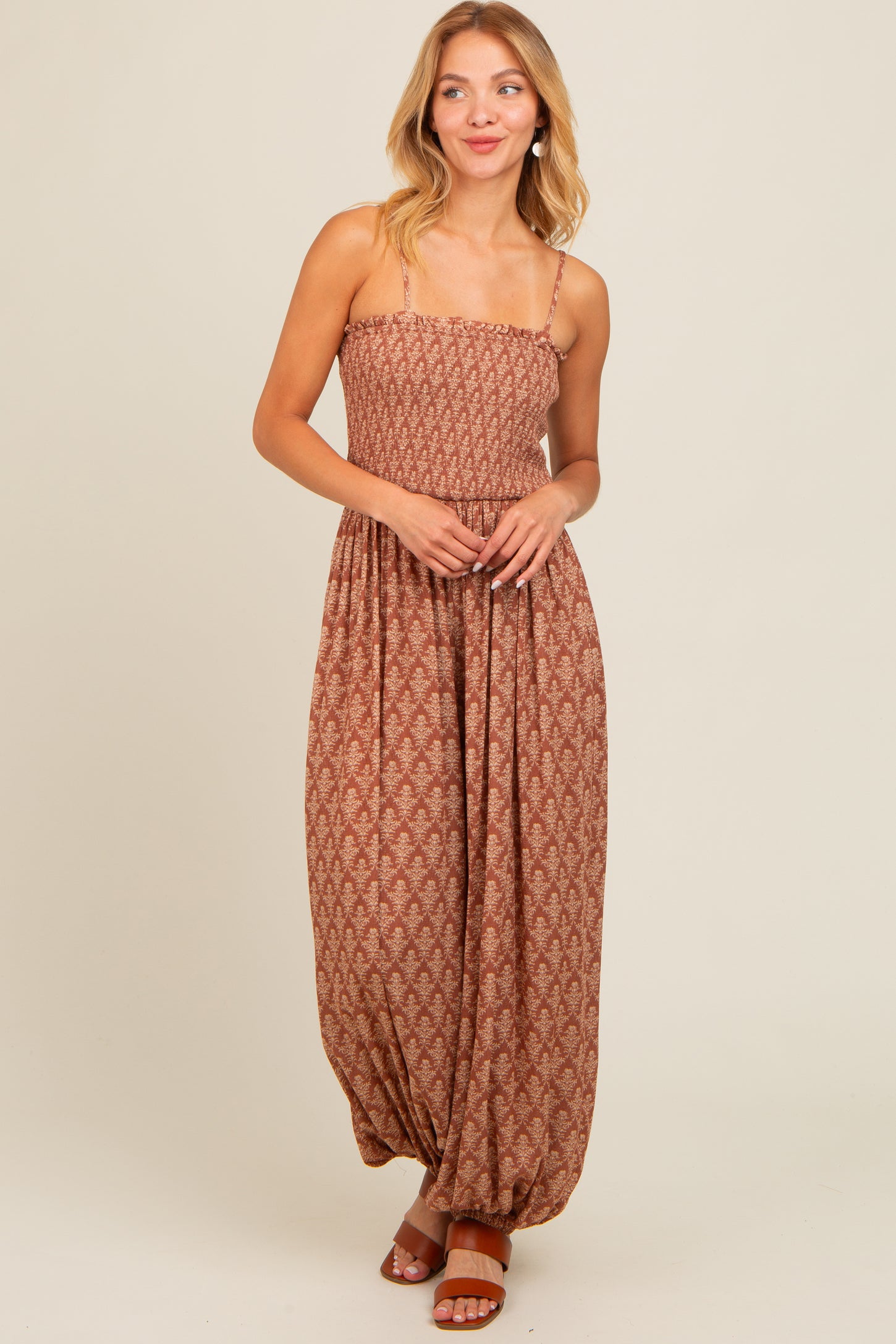 woman wearing a brown patterned maxi dress with spaghetti straps and a relaxed fit, standing and smiling