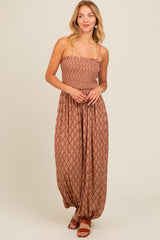 woman wearing a brown patterned maxi dress with spaghetti straps and a relaxed fit, standing and smiling