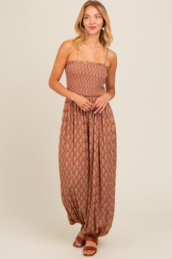 woman wearing a brown patterned maxi dress with spaghetti straps and a relaxed fit, standing and smiling