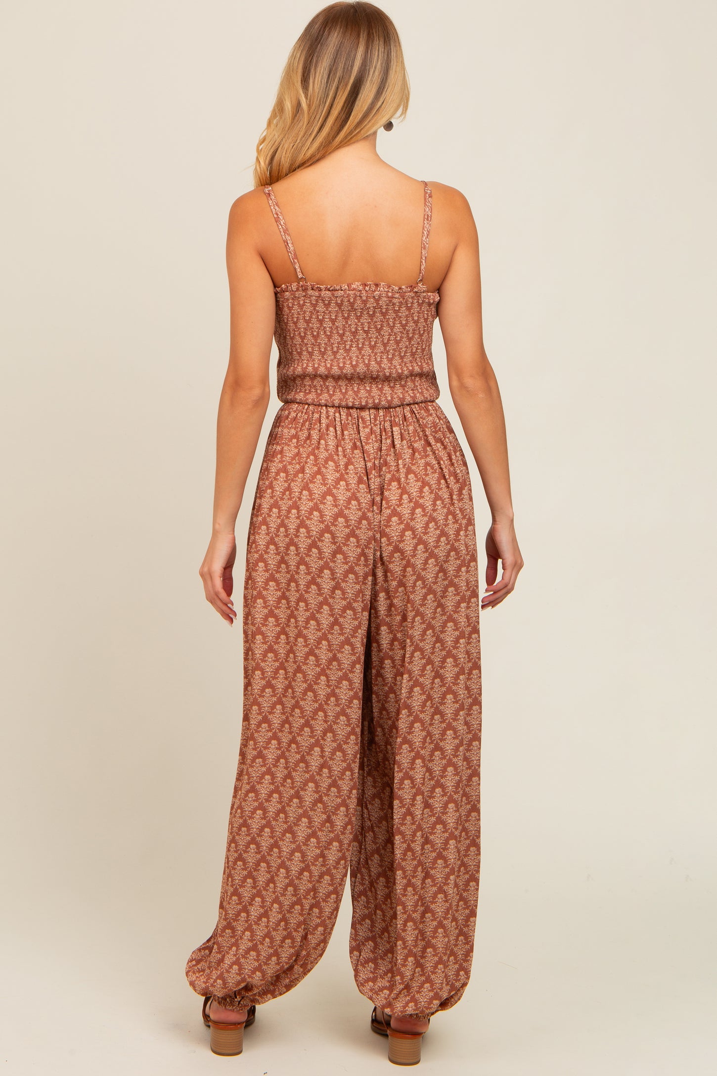 woman wearing a rust-colored, patterned jumpsuit with a fitted bodice and wide-leg pants, viewed from the back