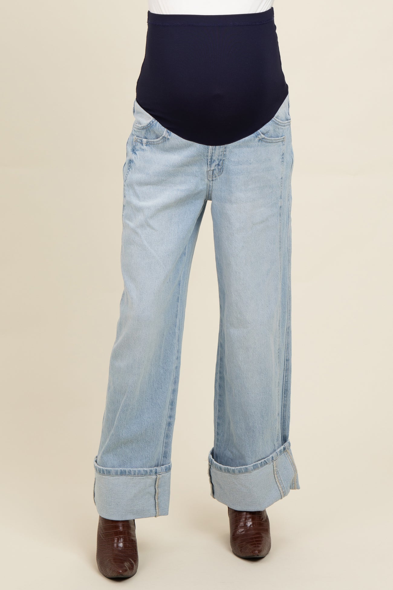 light blue maternity jeans with a dark blue over-the-bump waistband and rolled cuffs, styled with brown heeled boots