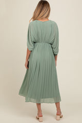 woman wearing a pleated sage green maternity dress with a gathered waist and flowy sleeves, turned away from the camera
