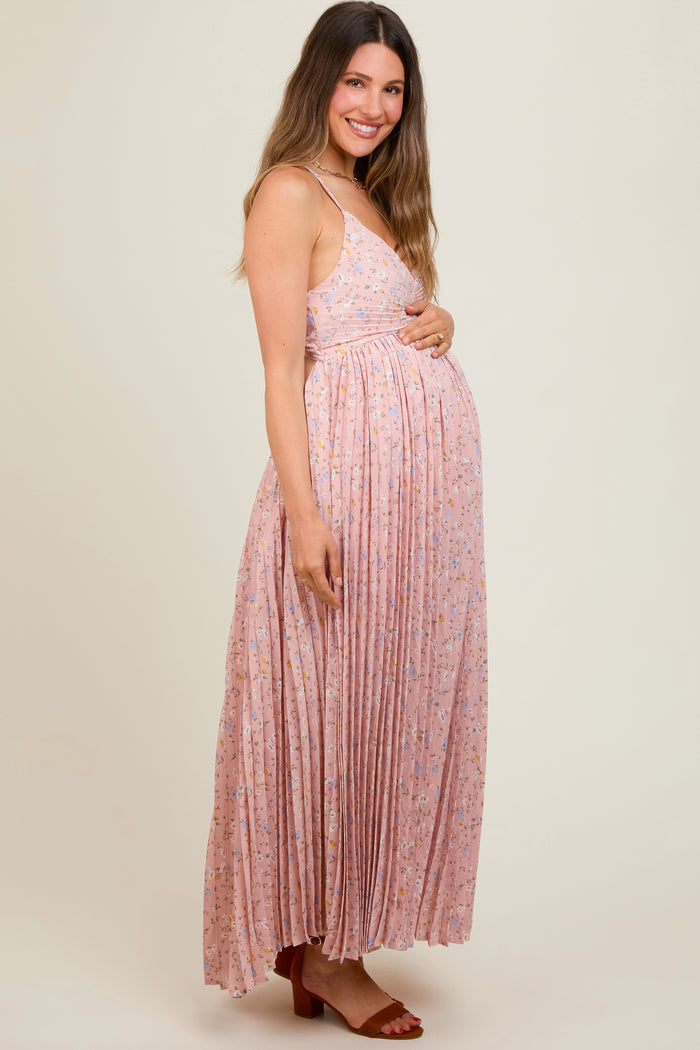 woman wearing a pink floral pleated maternity maxi dress and holding her baby bump