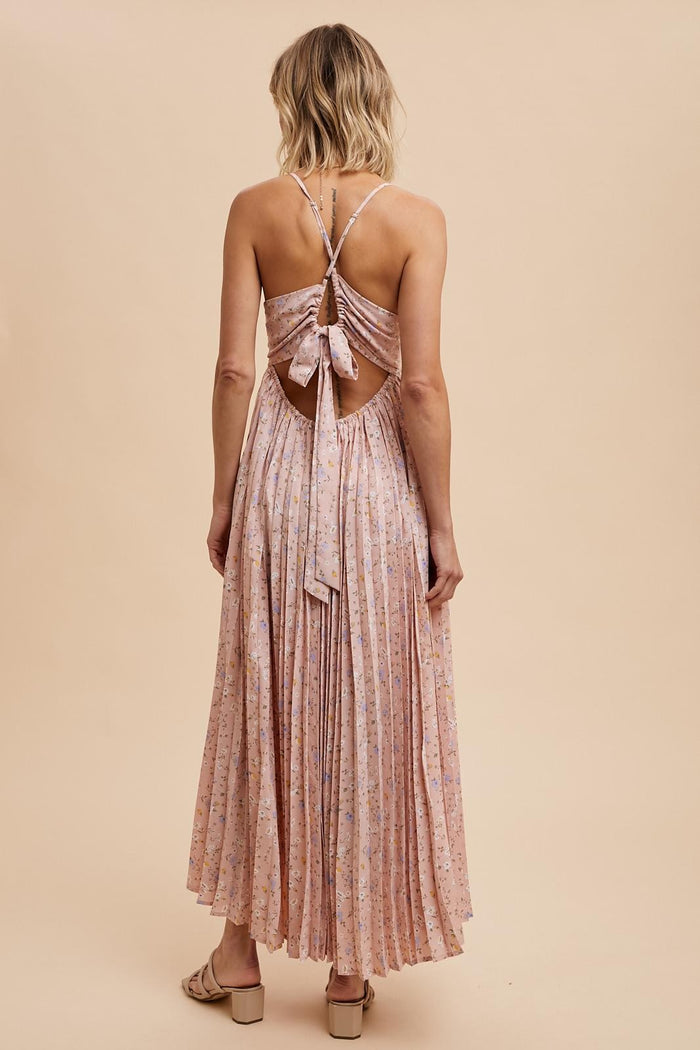 woman wearing a light pink pleated maxi dress with a tie-back detail and floral print, showing the back view