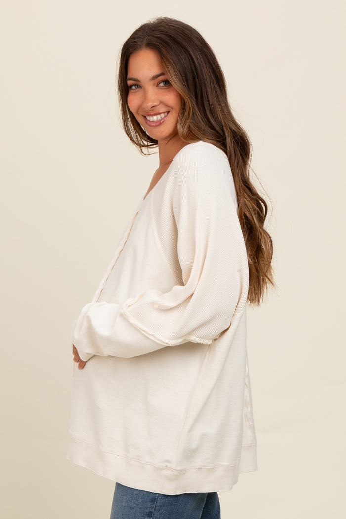 woman wearing a cream maternity top with puff sleeves and a v-neck, holding her baby bump