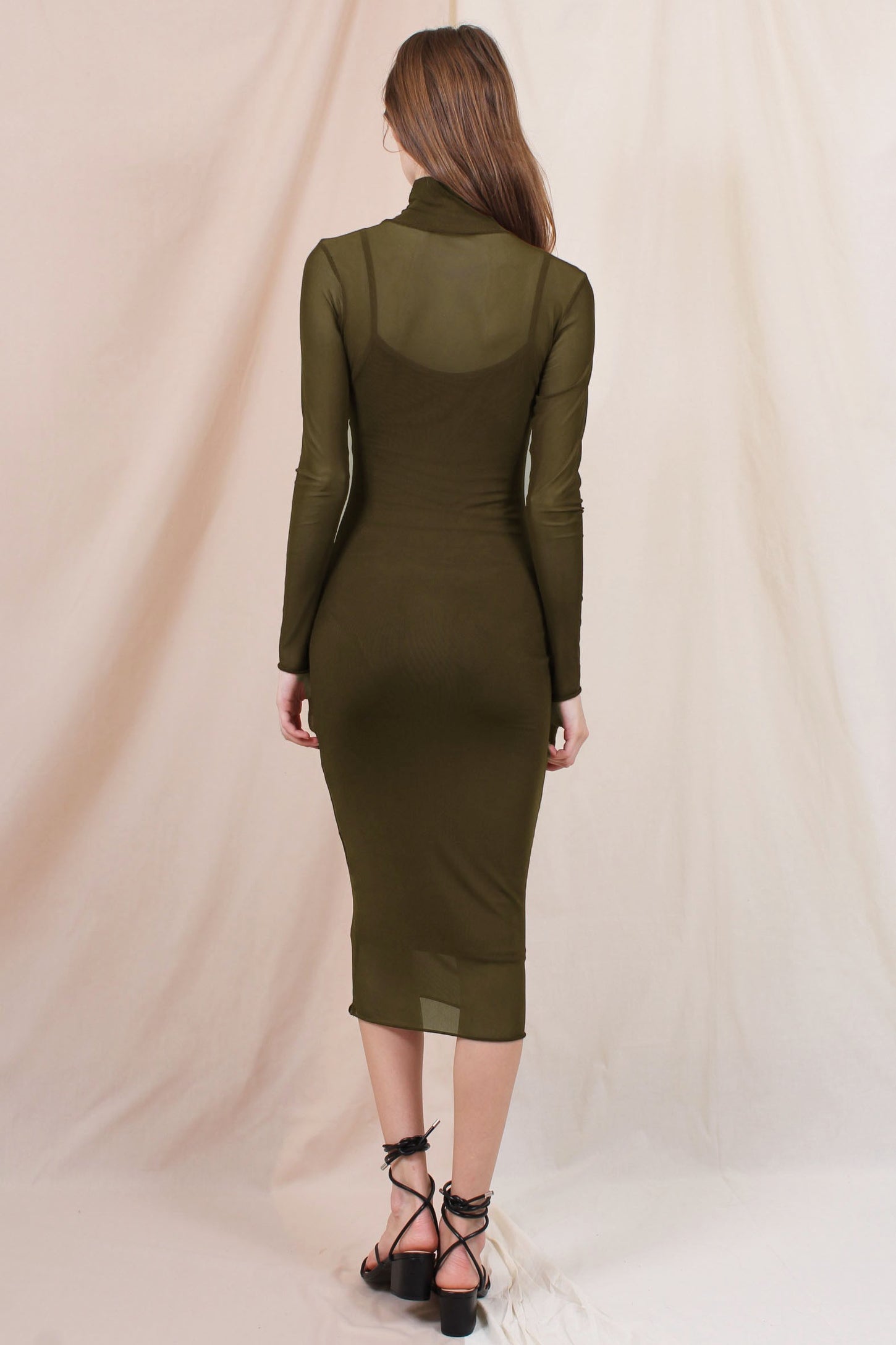 woman wearing a fitted olive green long sleeve midi dress with a sheer overlay and a mock neck