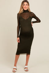 woman wearing a dark olive green maternity dress with a sheer long sleeve overlay and a visible baby bump