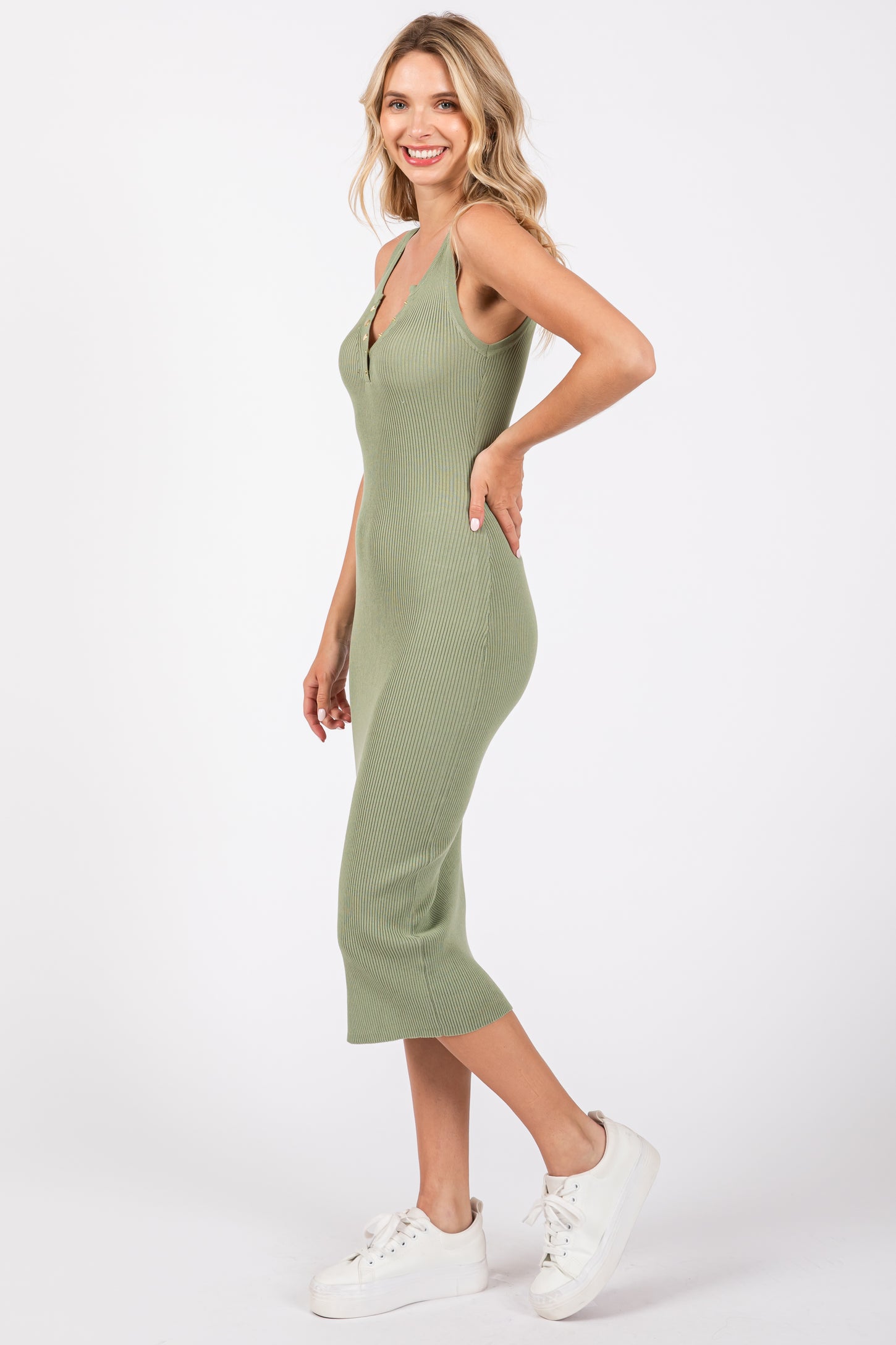 woman wearing a green ribbed midi dress with a v-neck and side slit, paired with white sneakers
