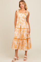 woman wearing a white floral tiered maxi dress with orange accents and ruffled straps
