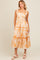 woman wearing a white floral tiered maxi dress with orange accents and ruffled straps
