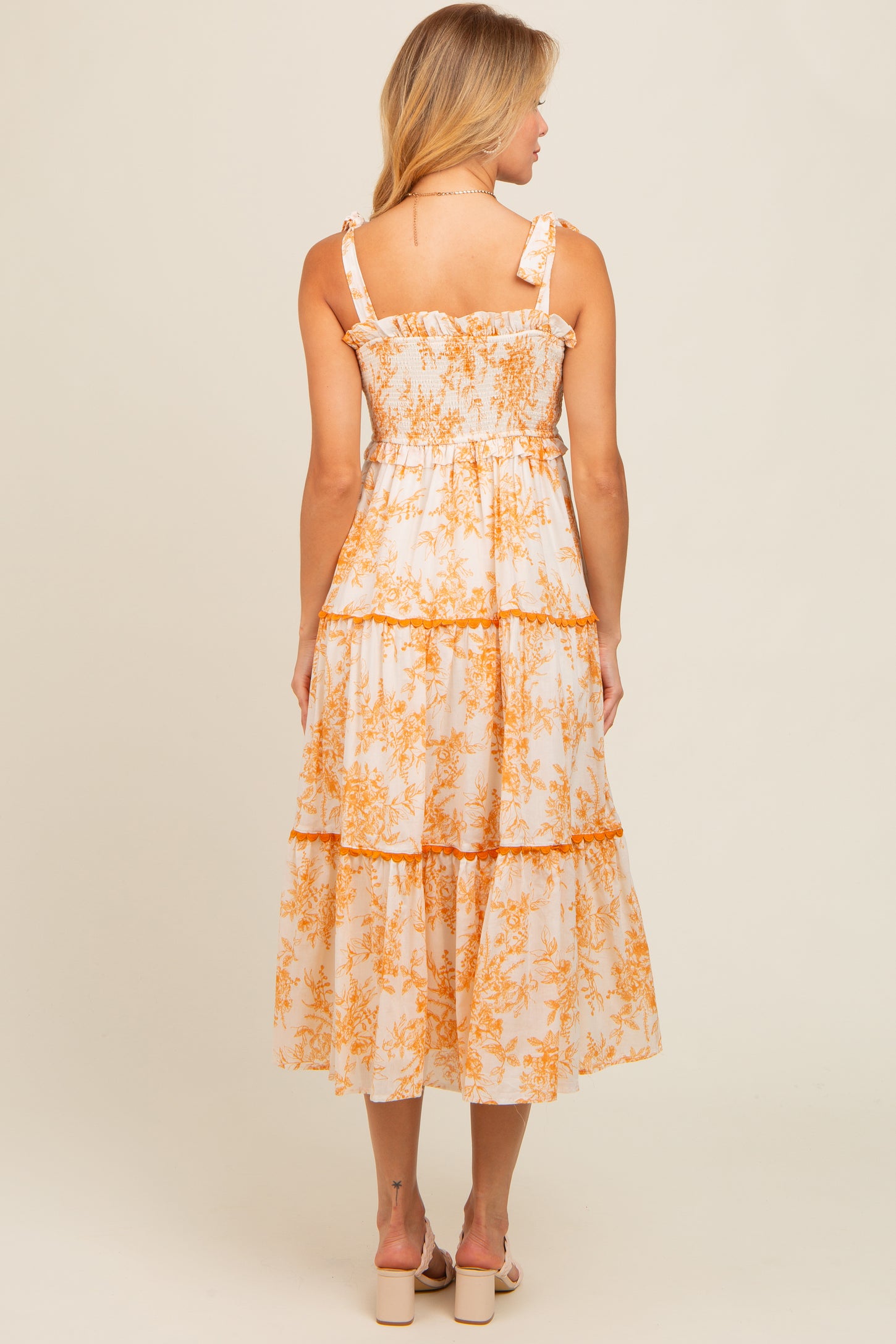 woman wearing a back view of a white midi dress with orange floral print and ruffled straps