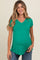woman wearing a green v-neck maternity top and showing her baby bump while smiling