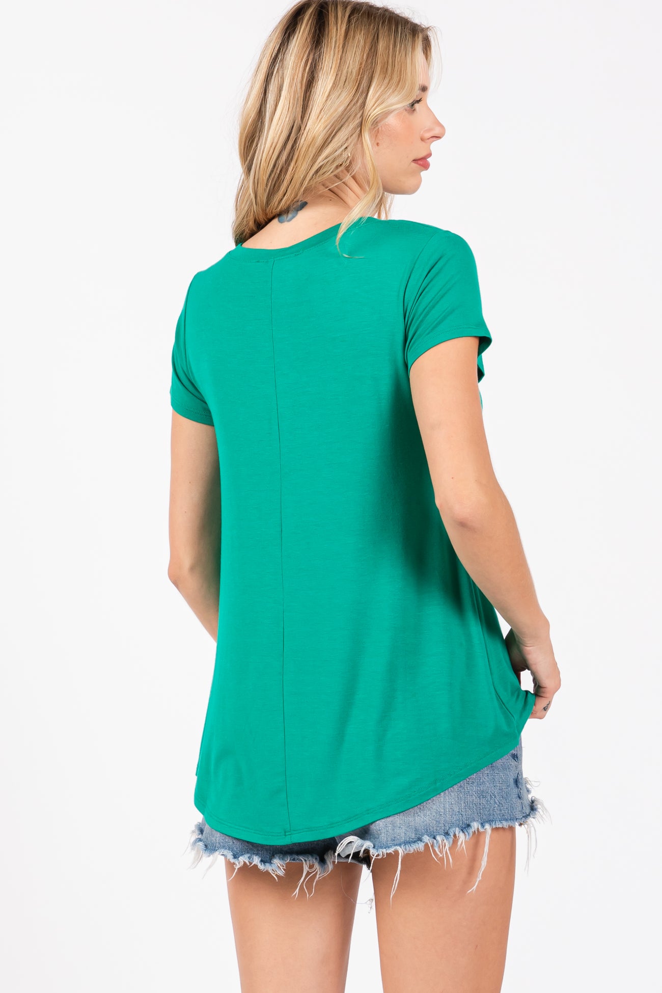 woman wearing a green short sleeve top paired with denim shorts, showing a relaxed fit and curved hemline