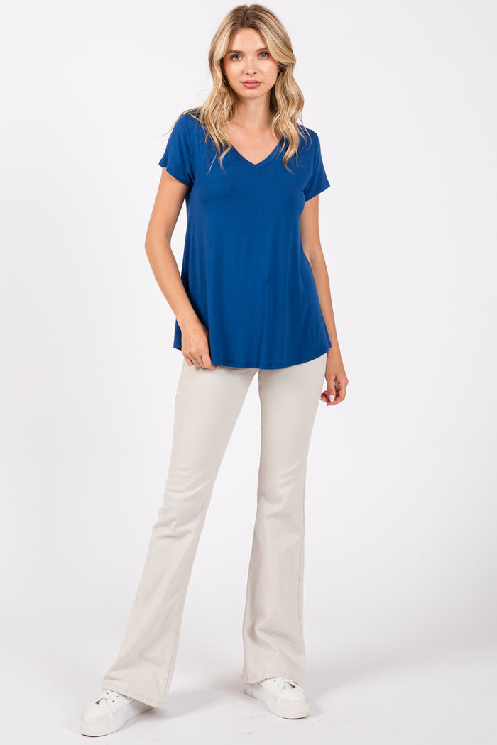 woman wearing a vibrant blue v-neck t-shirt and cream flared pants, standing against a white background