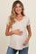 woman wearing a beige short sleeve maternity top and holding her baby bump