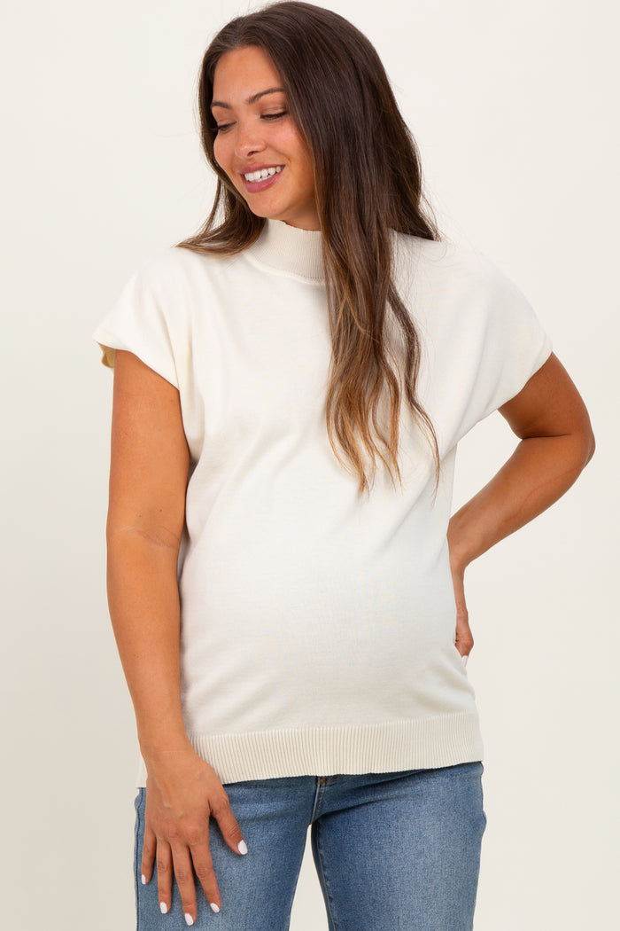 woman wearing a cream-colored short sleeve maternity top and blue jeans, showcasing her baby bump