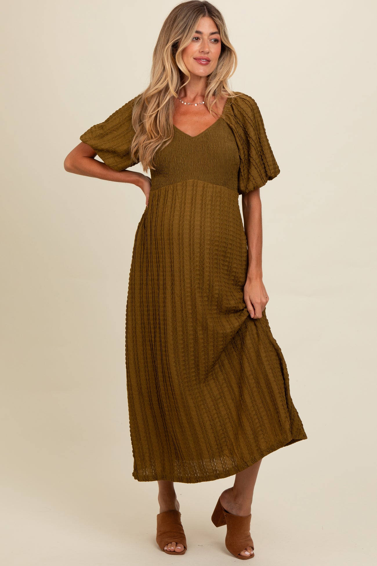woman wearing an olive green short sleeve maternity dress with a v-neckline and textured fabric, holding her baby bump