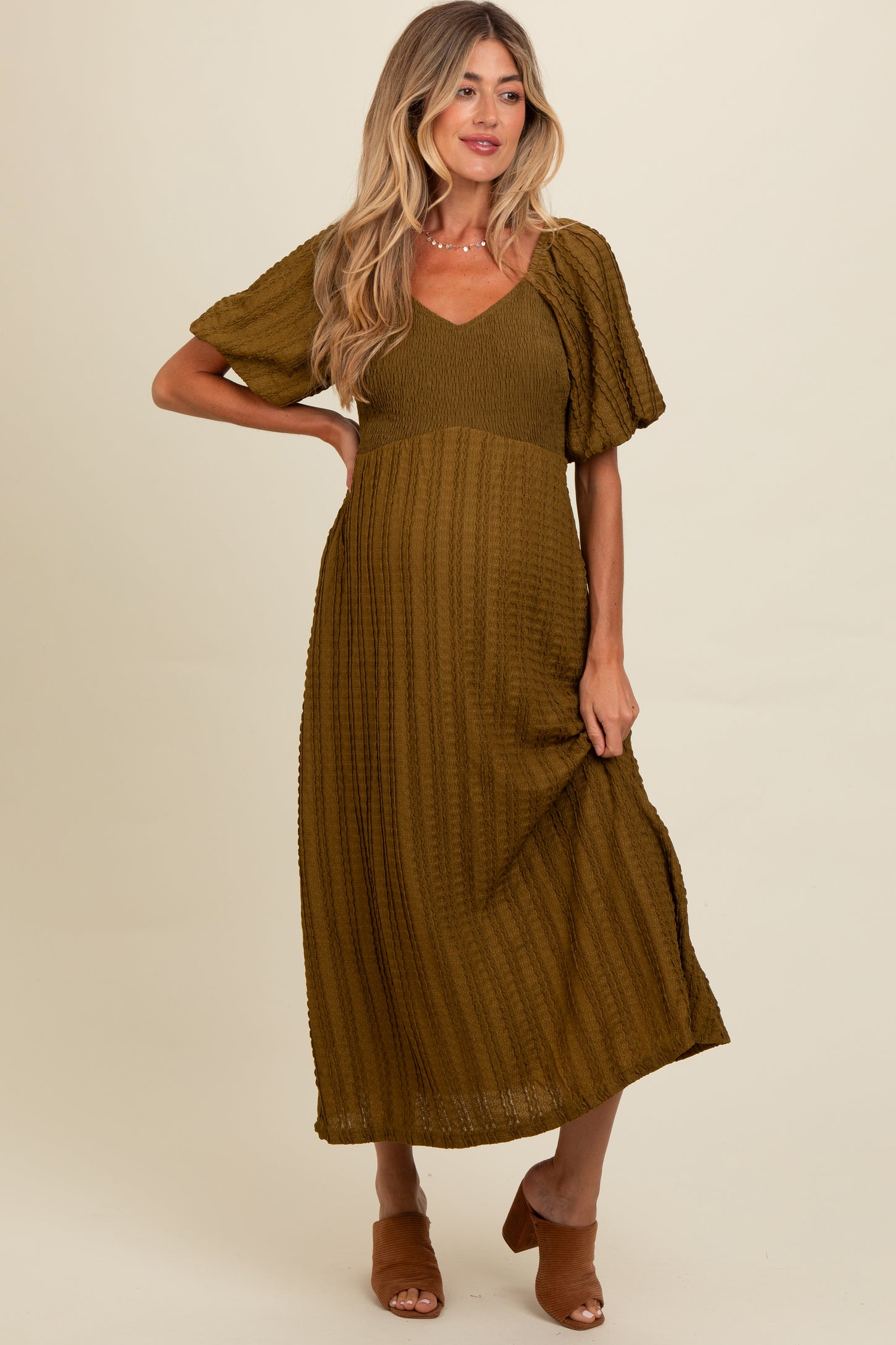 woman wearing an olive green short sleeve maternity dress with a v-neckline and textured fabric, holding her baby bump