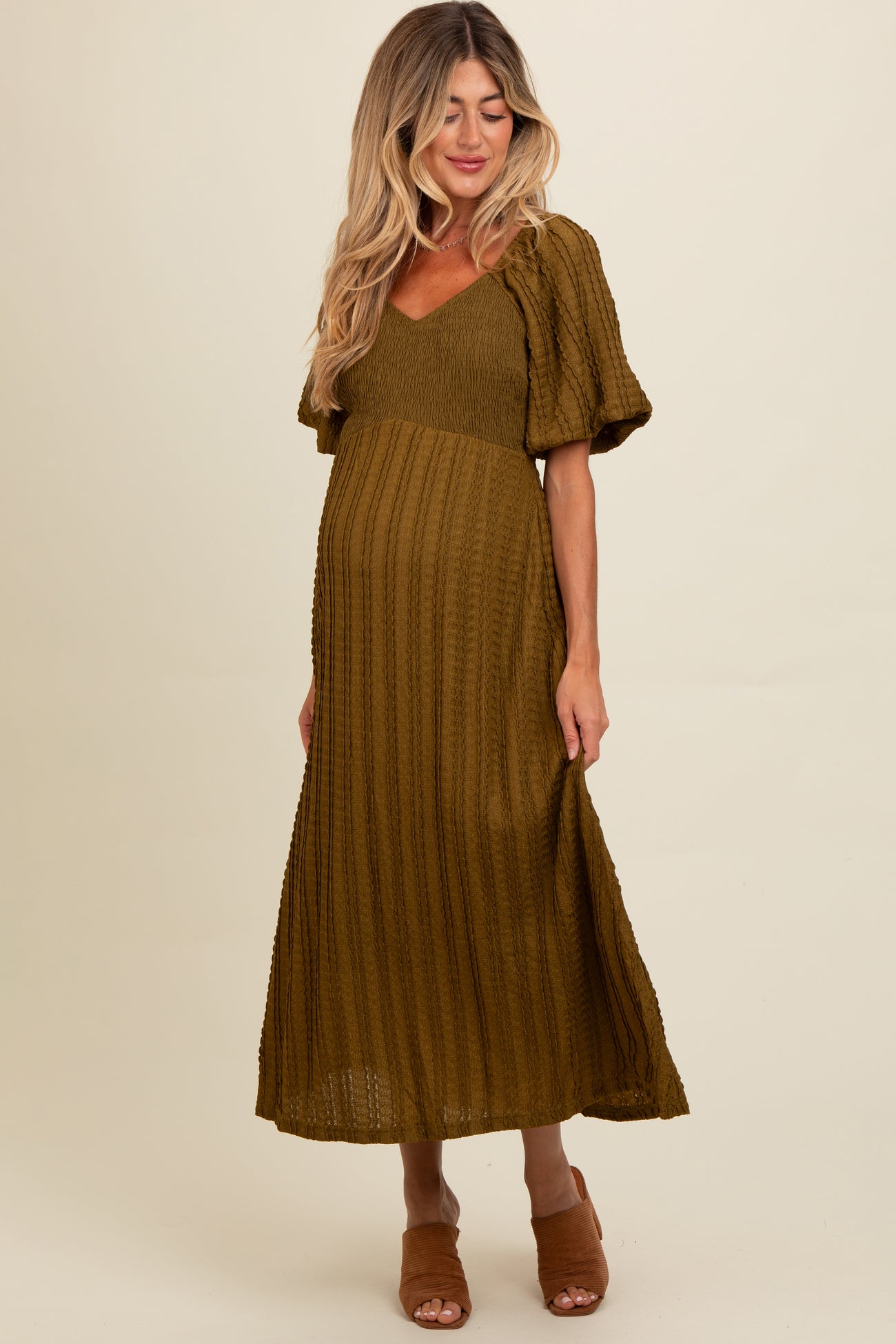 woman wearing an olive green maternity maxi dress with short puff sleeves and a fitted bodice, showcasing her baby bump