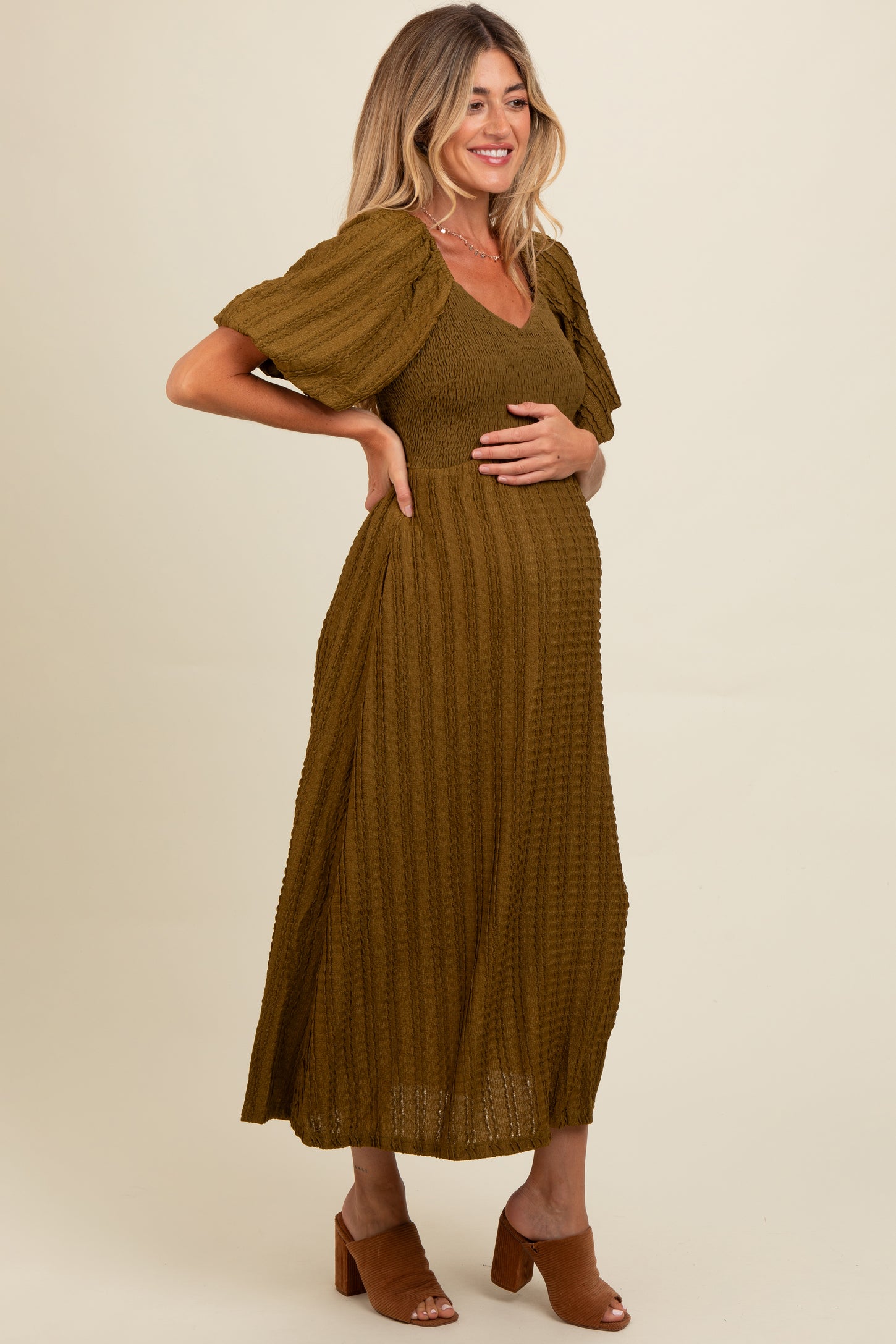 woman wearing a mustard green short sleeve maternity dress and holding her baby bump