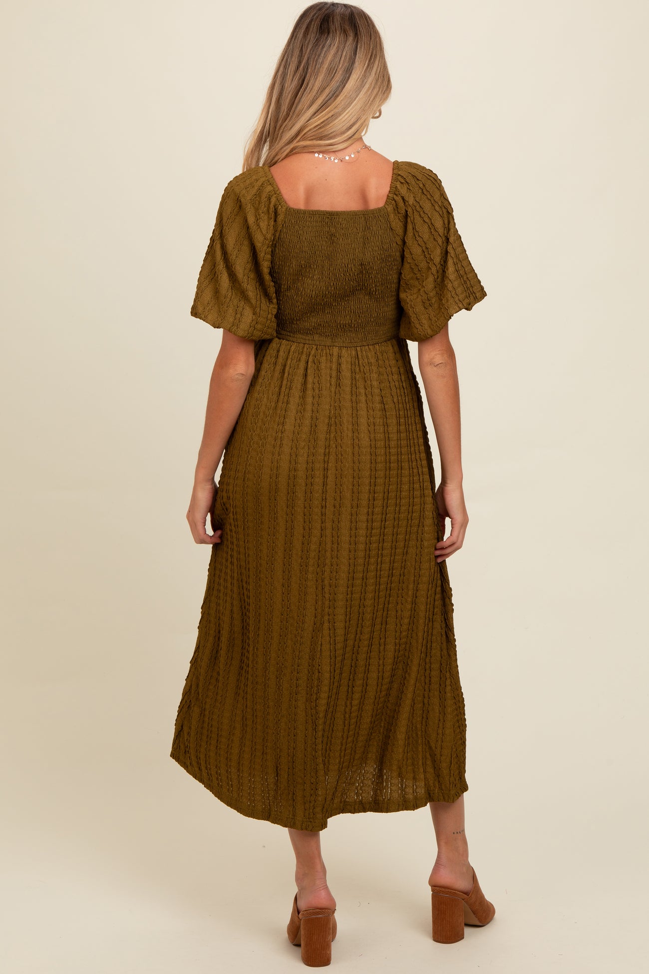 woman wearing a dark olive green maternity dress with a smocked bodice and short flutter sleeves, showing a pregnant belly