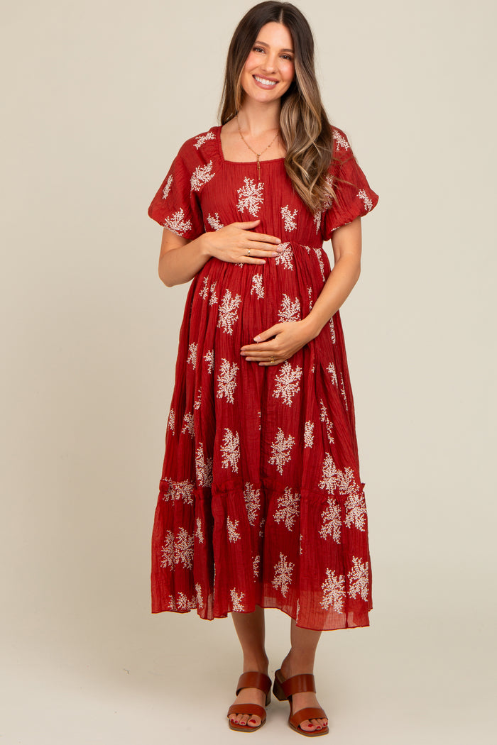 woman wearing a red maternity dress with white floral embroidery and holding her baby bump