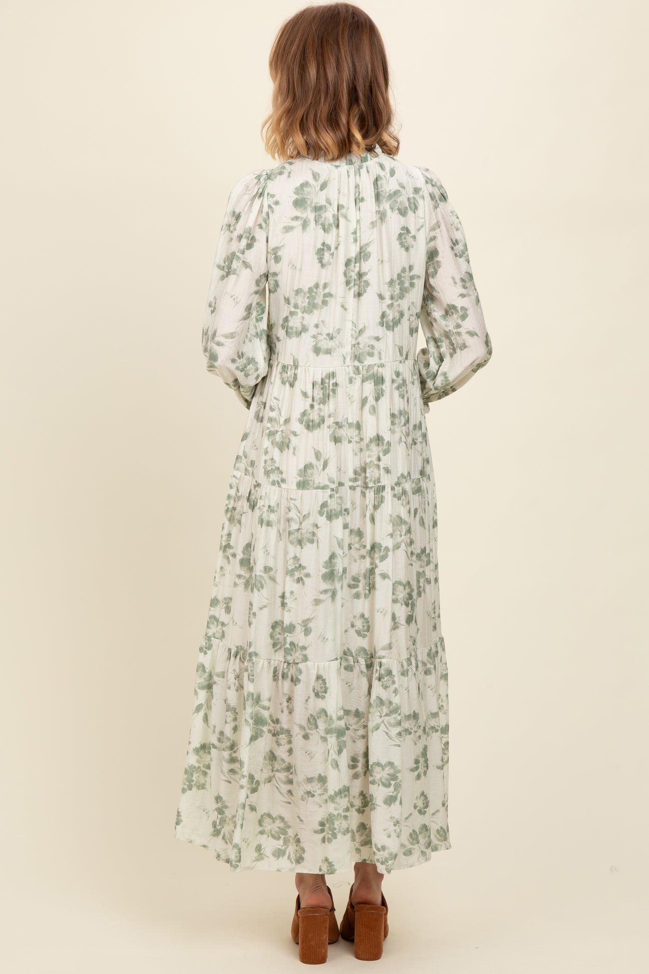 woman wearing a long green floral maxi dress with puff sleeves and a tiered skirt, viewed from the back