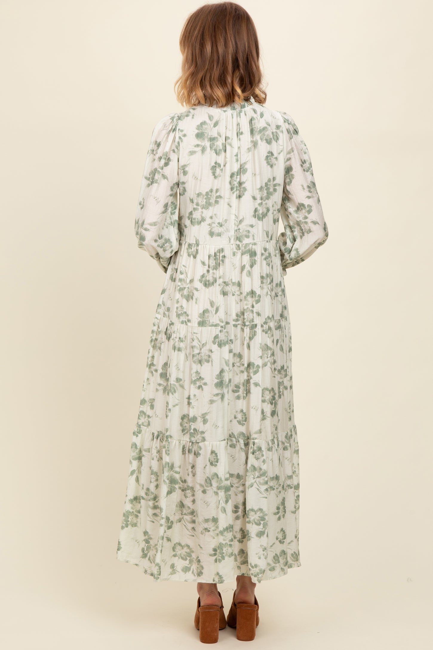 woman wearing a long green floral maxi dress with puff sleeves and a tiered skirt, viewed from the back