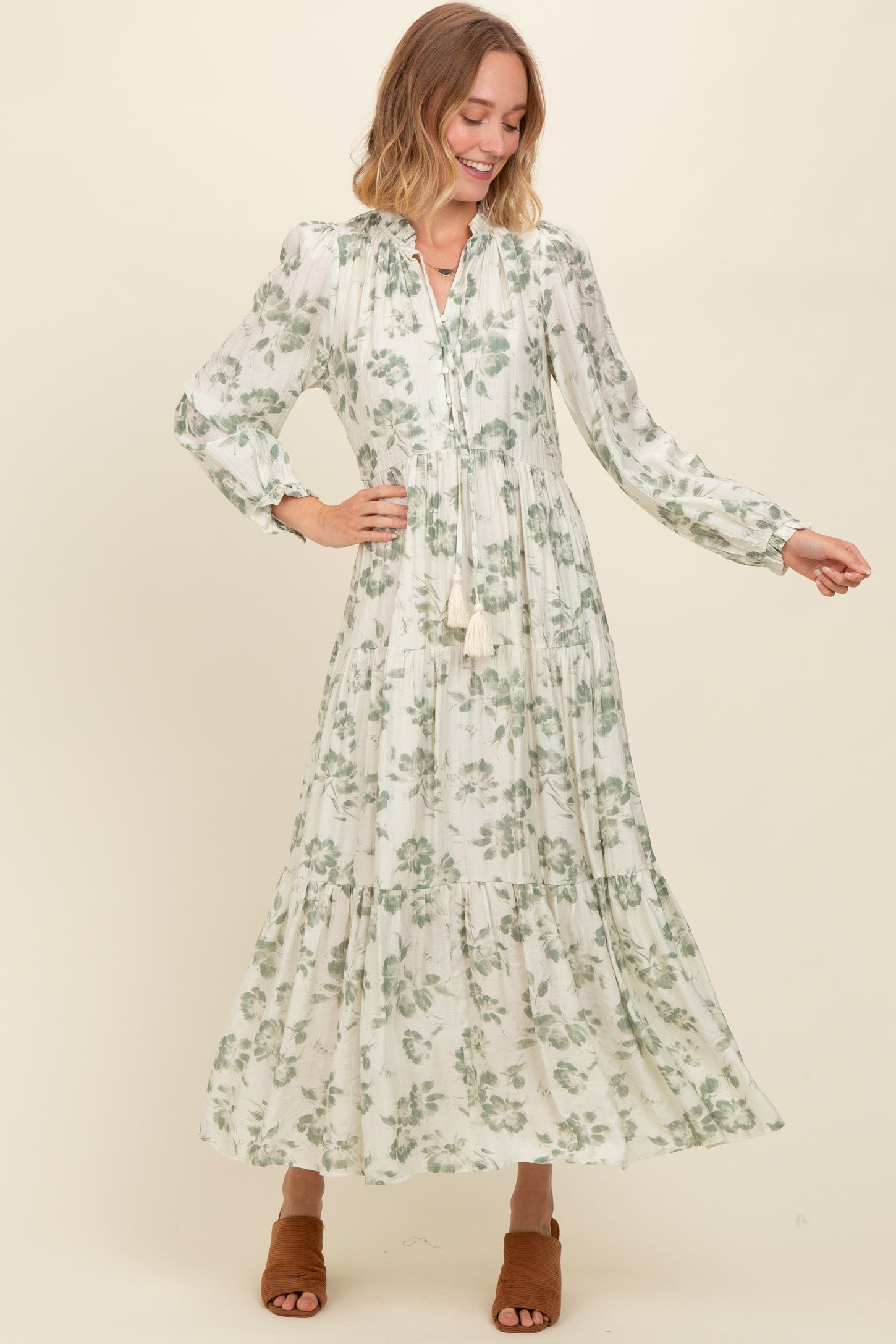 woman wearing a long sleeve floral maxi dress in white and green with a tiered design and tassel details